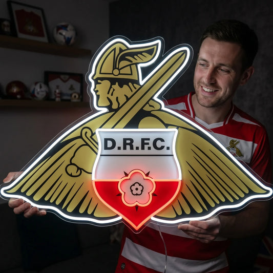 A man holding a custom-shaped Doncaster Rovers FC football club crest LED neon sign featuring the traditional Viking mascot with a shield and sword glowing in bright white, yellow, and red light