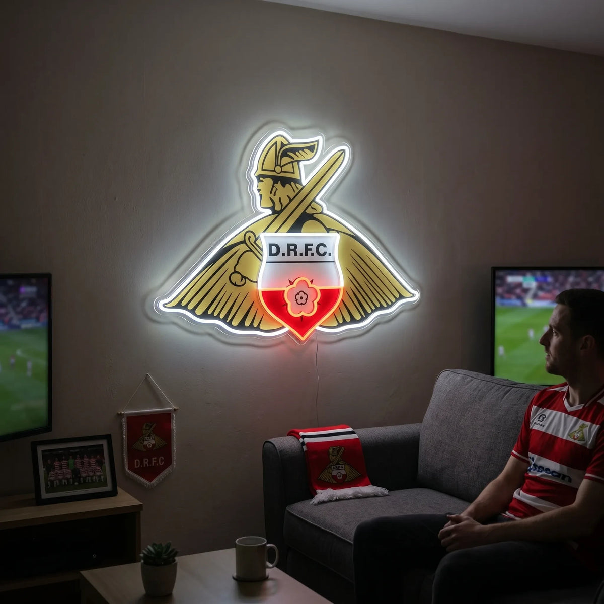 A man holding a custom-shaped Doncaster Rovers FC football club crest LED neon sign featuring the traditional Viking mascot with a shield and sword glowing in bright white, yellow, and red light