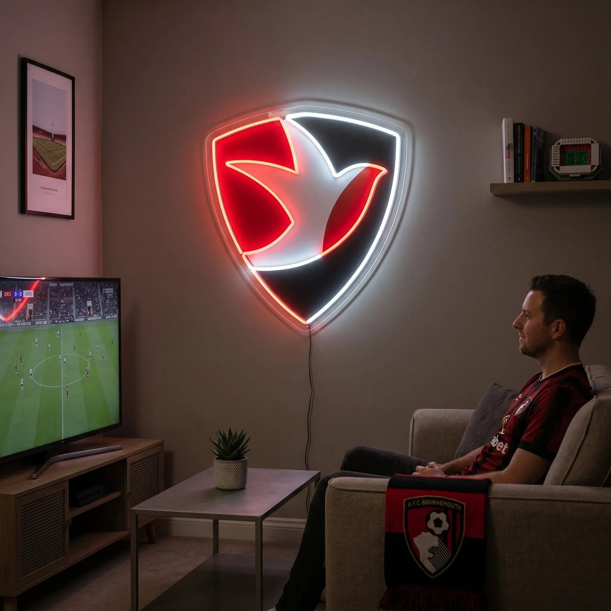 A man holding a shield-shaped AFC Bournemouth football club crest LED neon sign featuring the iconic stylized profile of Dickie Dowsett heading a football glowing in red and white light