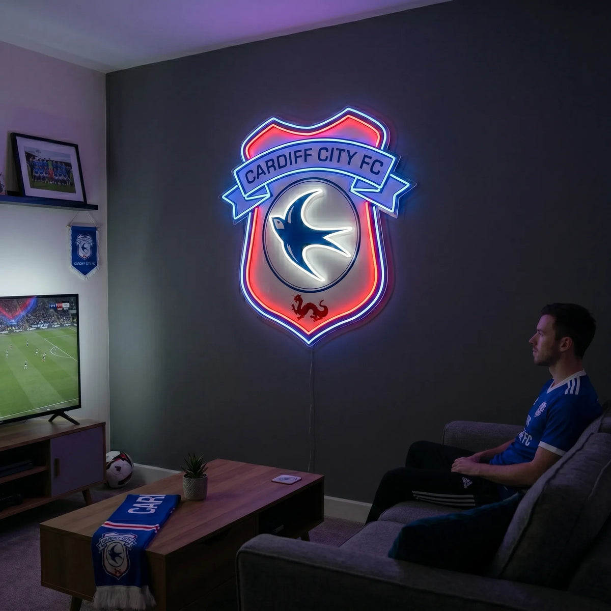 A man holding a shield-shaped Cardiff City FC football club crest LED neon sign featuring the iconic bluebird and red dragon glowing in blue, white, and red light