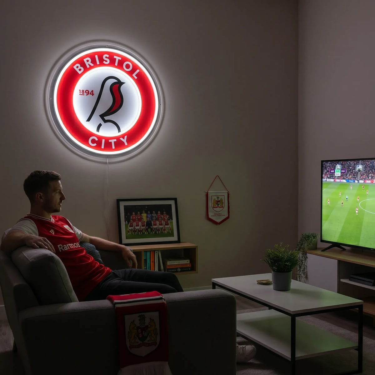 A man holding a circular Bristol City FC football club crest LED neon sign featuring the robin bird logo glowing in bright white and red light