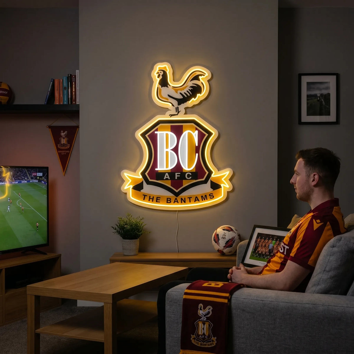 A man holding a custom Bradford City AFC football club crest LED neon sign featuring the BC initials, a bantam rooster on top, and The Bantams ribbon glowing in warm yellow and white light