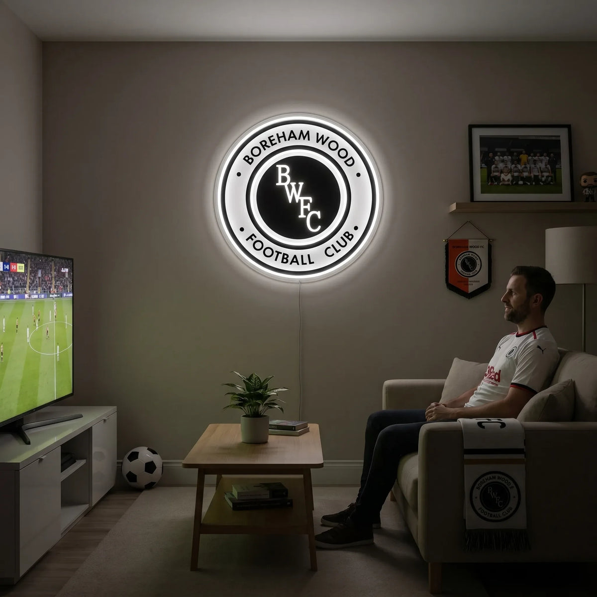 A man holding a large circular Boreham Wood FC football club crest LED neon sign with BWFC initials glowing in bright white light
