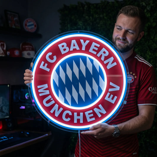 A man holding a large circular FC Bayern München football club crest LED neon sign glowing in bright blue and red light