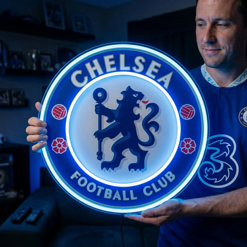 A man holding a large circular Chelsea Football Club crest LED neon sign featuring the iconic ceremonial lion rampant regardant holding a staff glowing in a vibrant blue and bright white light