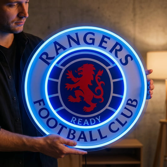 A man holding a large circular Rangers Football Club crest LED neon sign featuring the iconic red rampant lion in the center surrounded by the club's name glowing in vibrant blue light