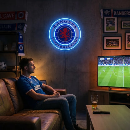 A man holding a large circular Rangers Football Club crest LED neon sign featuring the iconic red rampant lion in the center surrounded by the club's name glowing in vibrant blue light
