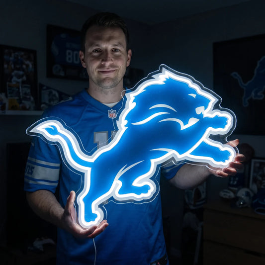 A smiling man holding a large custom-shaped Detroit Lions NFL football team logo LED neon sign featuring the iconic leaping lion silhouette glowing in a vibrant Honolulu blue and bright white light