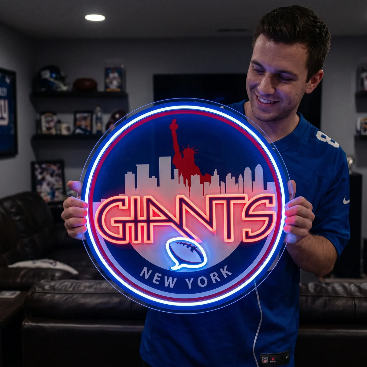 A smiling man holding a large circular New York Giants NFL football team themed LED neon sign featuring a red Statue of Liberty and city skyline silhouette above the stylized red Giants wordmark and a glowing blue football symbol