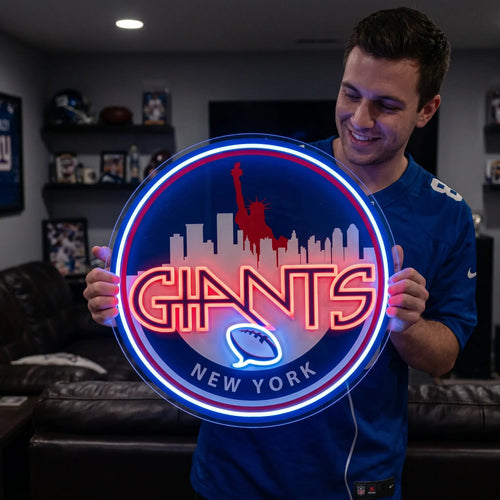 A smiling man holding a large circular New York Giants NFL football team themed LED neon sign featuring a red Statue of Liberty and city skyline silhouette above the stylized red Giants wordmark and a glowing blue football symbol
