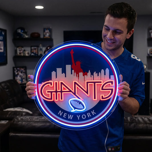 A smiling man holding a large circular New York Giants NFL football team themed LED neon sign featuring a red Statue of Liberty and city skyline silhouette above the stylized red Giants wordmark and a glowing blue football symbol