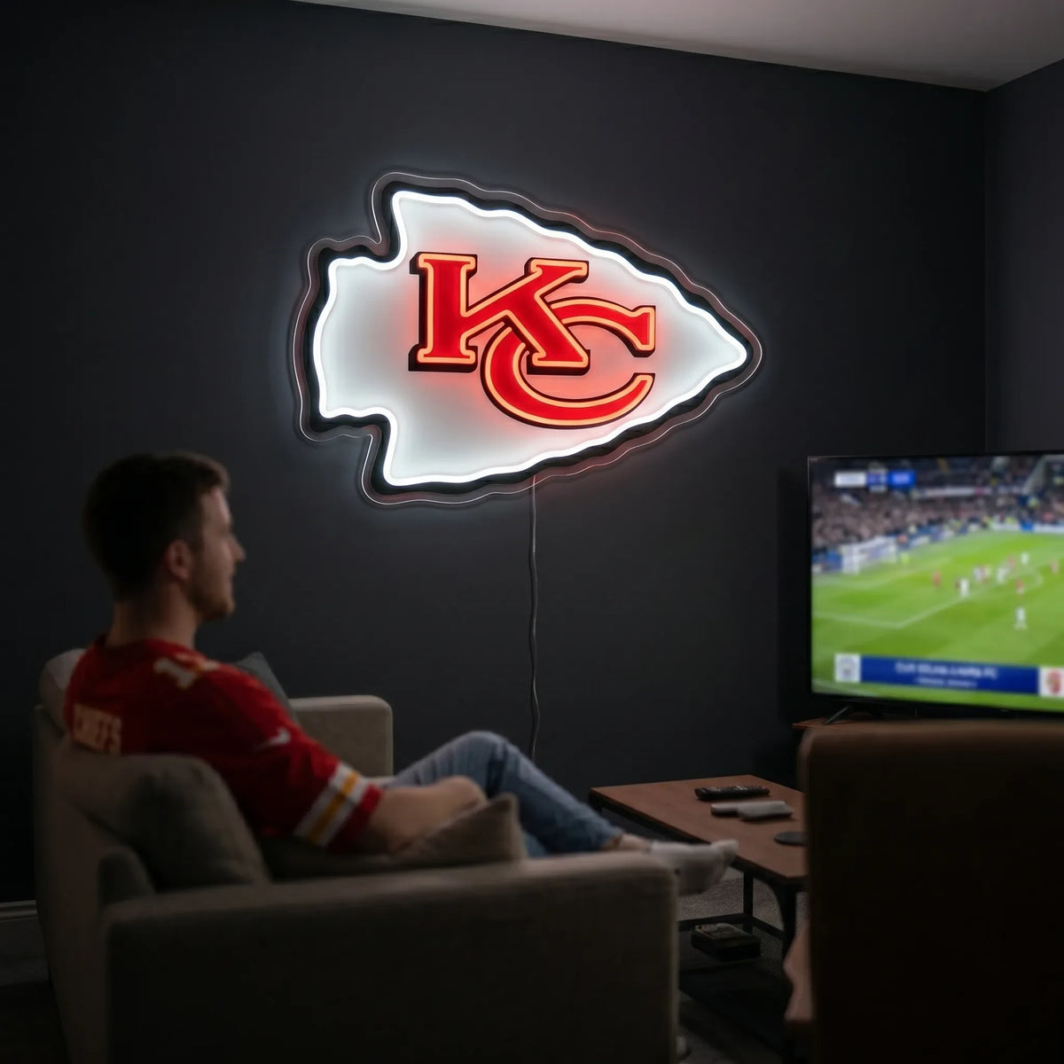 A man holding a large arrowhead-shaped Kansas City Chiefs NFL football team logo LED neon sign featuring the interlocking KC monogram in red with a bold black outline glowing in vibrant red and bright white light
