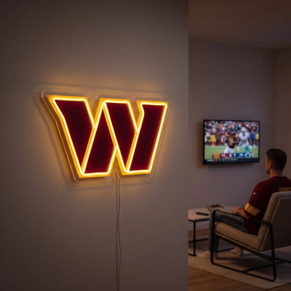 A man holding a large custom-shaped Washington Commanders NFL football team logo LED neon sign featuring the bold stylized letter W in burgundy outlined by a glowing vibrant yellow gold light