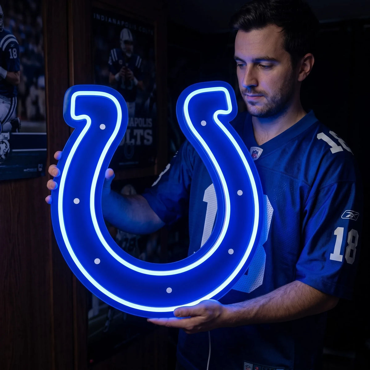 A man holding a large custom-shaped Indianapolis Colts NFL football team logo LED neon sign featuring the iconic blue horseshoe with seven white dots glowing in a vibrant blue light