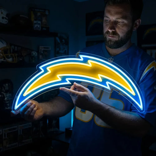 A man holding a large custom-shaped Los Angeles Chargers NFL football team logo LED neon sign featuring the iconic curved lightning bolt glowing in vibrant yellow and powder blue light