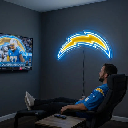 A man holding a large custom-shaped Los Angeles Chargers NFL football team logo LED neon sign featuring the iconic curved lightning bolt glowing in vibrant yellow and powder blue light