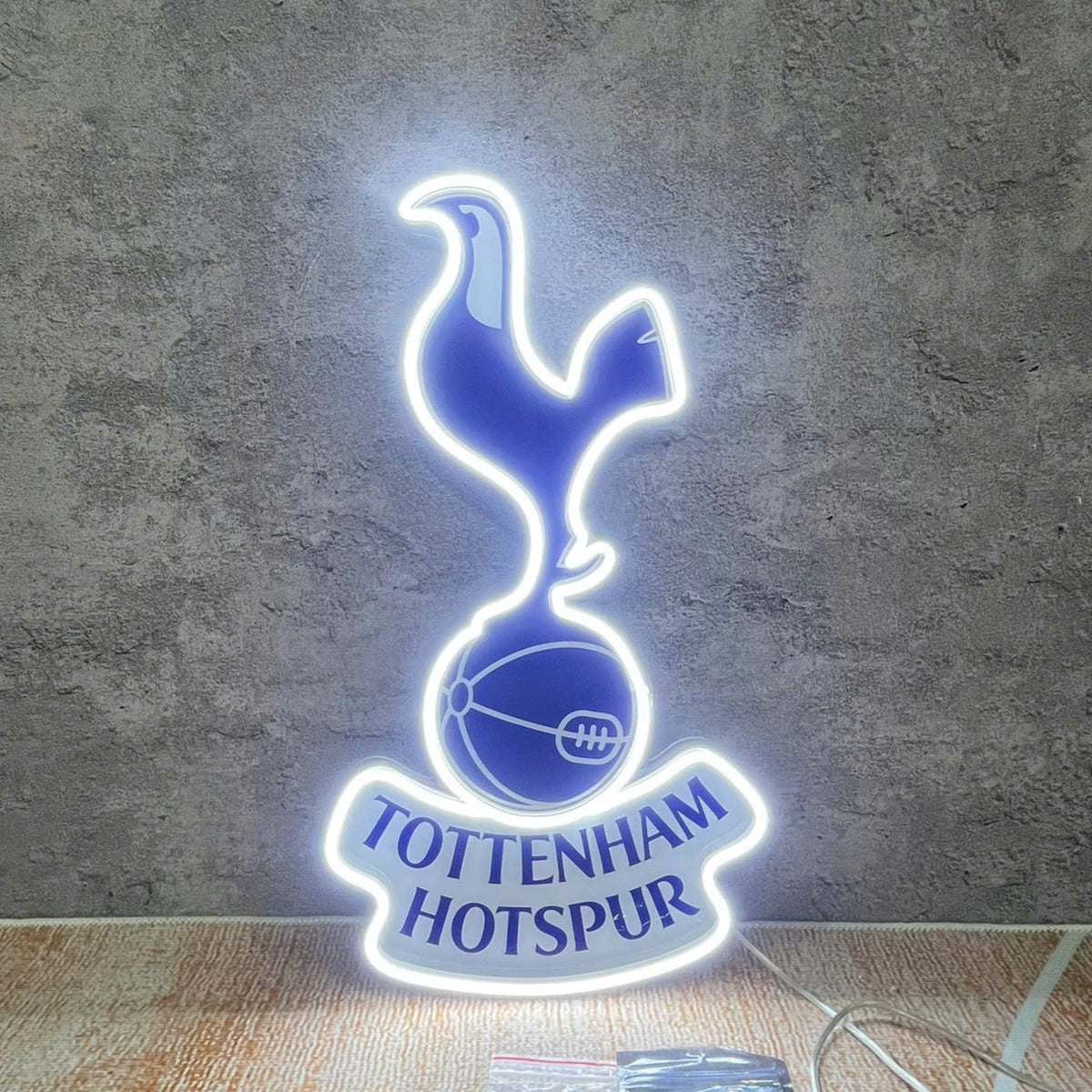 Vibrant white and blue LED Neon Sign of Tottenham Hotspur FC crest glowing on a dark wall background